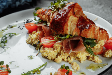 Delicious croissant sandwich with ham, cheese and scrambled eggs on plate served
