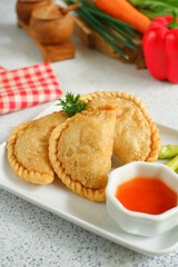 a plate of fried pastries containing vegetables served with sauce against white background
