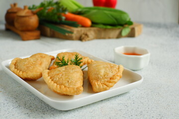 a plate of fried pastries containing vegetables served with sauce against white background 