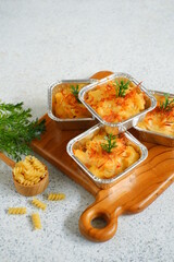 selective focus of  baked macaroni and cheese  in aluminium foil cup against white background 