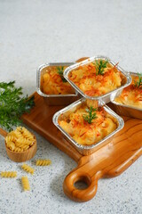 selective focus of  baked macaroni and cheese  in aluminium foil cup against white background 