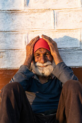portrait of an old indian man, old aged man with wrinkles on his face holding his face with his hands and sitting in the sunlight.