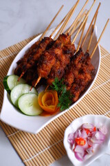 a plate of grilled chicken in bamboo skewer named satay against white background