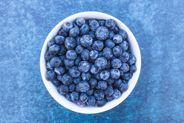 Bowl of fresh blueberries isolated on blue background.