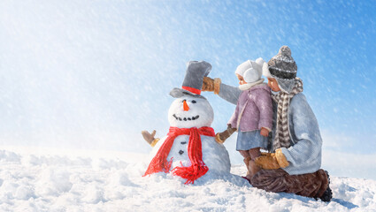 Children make a beautiful snowman on a sunny winter day. Happy boy and girl in rustic style are...