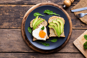 Sliced Avocado on Whole Wheat Toast, Avocado Sandwich with Fried Egg On black plate on the wooden table
