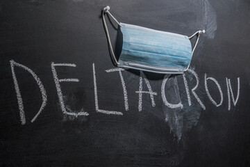 A blue medical mask hangs over the word Deltacron written in chalk on the board. Deltacron is the...