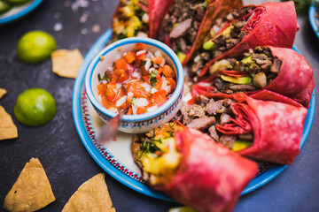 Six delicious burritos and cup of pico de gallo on dark surface