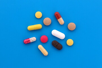 A pile of medicines of different sizes and colors lie on a blue background. - Powered by Adobe