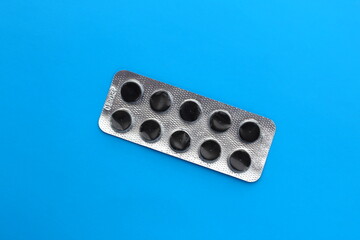 Black pills lie in one tablet on a blue isolated background.