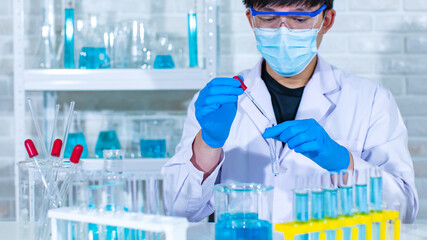 Closeup facial shot of Asian young professional male scientist in white lab coat wearing safety protection goggles glasses using microscope lens looking zooming at microbiology sample on glass plate