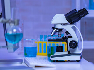 Closeup studio shot of magnifier zooming lens microscope camera placing on working table in hospital laboratory full of glassware equipment test tube rack Erlenmeyer flask beaker and computer monitor