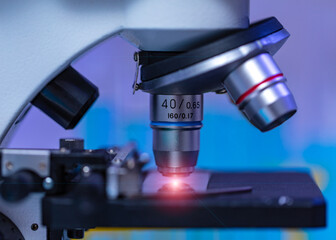 Closeup studio shot of magnifier zooming lens microscope camera placing on working table in hospital laboratory full of glassware equipment test tube rack Erlenmeyer flask beaker and computer monitor