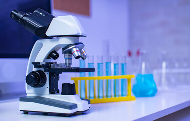 Closeup studio shot of magnifier zooming lens microscope camera placing on working table in hospital laboratory full of glassware equipment test tube rack Erlenmeyer flask beaker and computer monitor