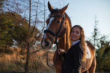 Young woman with curly hair petting her horse in a sunny morning