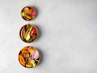 Dehydrated vegan chips in a wooden mango bowl. Vitamin healthy fast food with carrot slices, beetroot wedges, broccoli, zucchini on a light table. food photo banner copy space.