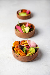 Dehydrated vegan chips in a wooden mango bowl. Vitamin healthy fast food with carrot slices, beetroot wedges, broccoli, zucchini on a light table. food photo banner copy space.