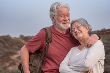 Loving mature adult gray-haired Caucasian senior adult couple embracing on outdoor excursion. Two smiling relaxed seniors enjoying freedom and a healthy lifestyle in nature during their retirement