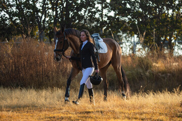 Young woman with curly hair walking with her horse in a sunny morning