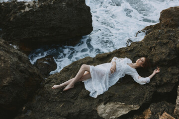 Beautiful bride Lies on his back on a stone cliff, cloudy weather vacation concept