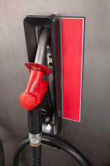 A red fuel nozzle set in the fuel pump, at a petrol station.