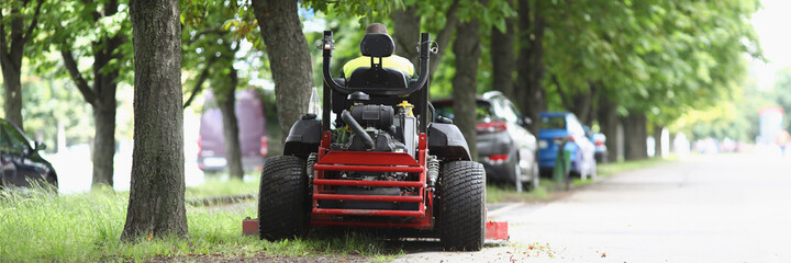 The lawn mower stands on sidewalk near the lawn - obrazy, fototapety, plakaty