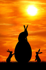 Silhouettes of three hares, a hare sits on a large Easter egg against the backdrop of sunset