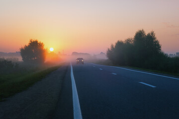 Car Drives On The Suburban Road On A Foggy Morning During Golden Sunrise