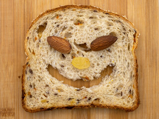 Funny animal face made from a slice of multigrain bread,  almonds and raisins. Joyful healthy food on wooden background.
