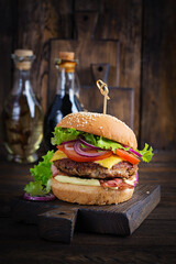 Hamburger with bacon, turkey burger meat, cheese, tomato and lettuce on wooden background. Tasty...