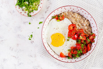 Breakfast oatmeal porridge with roasted egg and tomatoes salad. Healthy balanced food. Top view, above