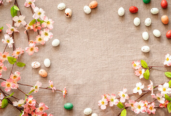 Top view of Easter eggs and flowers on a beige background. Easter eggs and blooming branches on a textured beige linen background