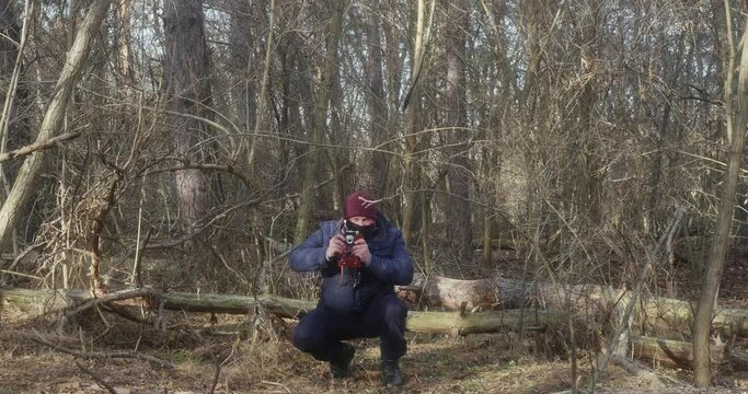 a man in a beautiful pine forest takes pictures of squatting on a film camera