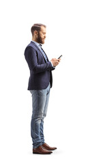 Full length profile shot of a man in suit and jeans typing on a mobile phone