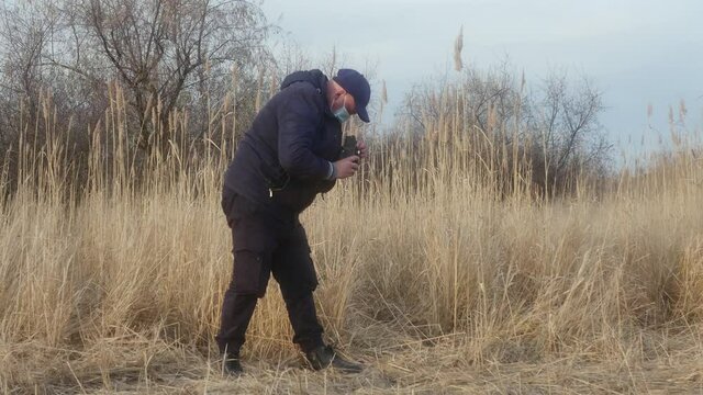 a traveler-photographer in a protective mask on his face, photographing nature on a two-lens reflex camera against a background of reeds