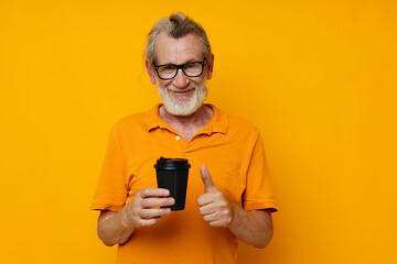 elderly man in a yellow T-shirt a glass with a drink yellow background