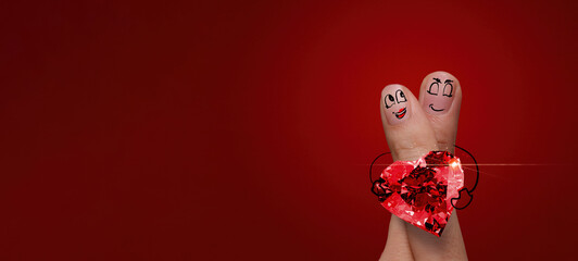 the happy finger couple in love with painted smiley and hold diamond ring heart shape on red background.
