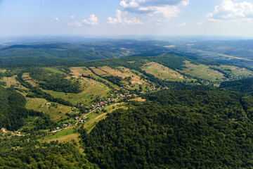 Aerial view of mountain hills covered with dense green lush woods on bright summer day