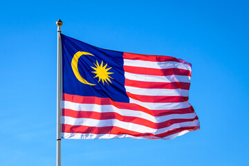 The national flag of Malaysia is flying in the wind at full mast against blue sky.