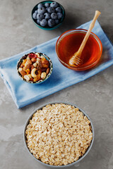 Healthy breakfast oatmeal with berries, nuts and honey. Oat flakes, blueberries, honey and assorted nuts on a gray background. Vegan breakfast with oatmeal. Top view