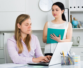 Female senior manager examining work of woman newcomer in office