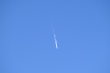 Distant passenger jet plane flying on high altitude on clear blue sky leaving white smoke trace of contrail behind. Air transportation concept