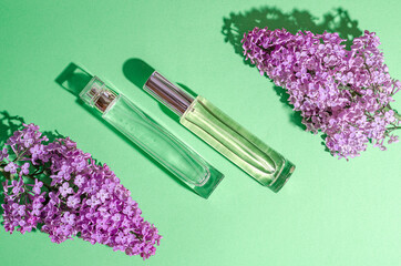 Purple lilac flowers and a two glass bottle with perfume on a green background. Bright shadows and light. Place for your text. Flat lay.