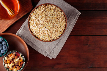 Dry oatmeal flakes, blueberries, honey and assorted nuts on a wooden background. Cereal and various delicious ingredients for breakfast on a boards. Copy space. Top view
