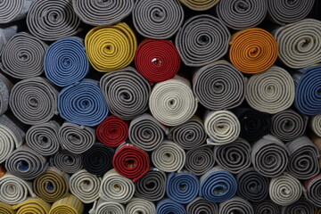 Carpets in different colors and patterns that are rolled up and stacked on top of each other.