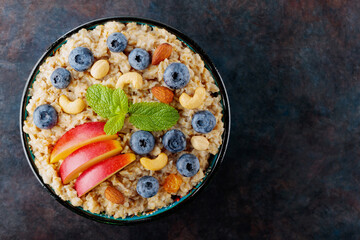 Oatmeal porridge with blueberries, apple slices and nuts. Bowl of oatmeal on dark background. Vegetarian food concept. Healthy food. Copy space. Top view