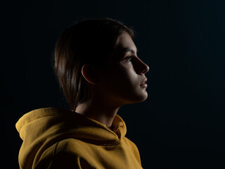 A young brunette woman looks up, a dreamer, silhouette on a dark background, studio portrait.
