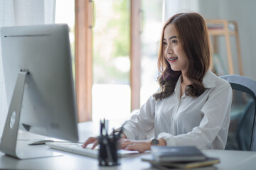 Portrait of smiling beautiful business Asian woman with working in modern office desk using computer, Business people employee freelance online marketing e-commerce telemarketing concept.