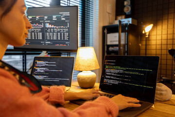 Woman writing programming code on laptops and desktop computer at cozy home workplace. Concept of...