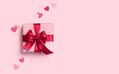 Pink gift box with red bow on pink background with hearts decoration around. Top view. Flat lay.